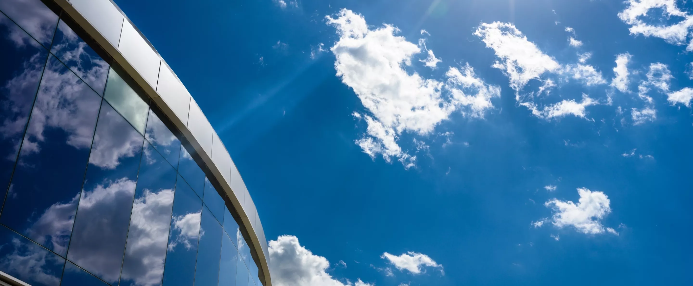 Upper floor of the Belknap Academic Building with blue sky and clouds reflected off of the exterior.