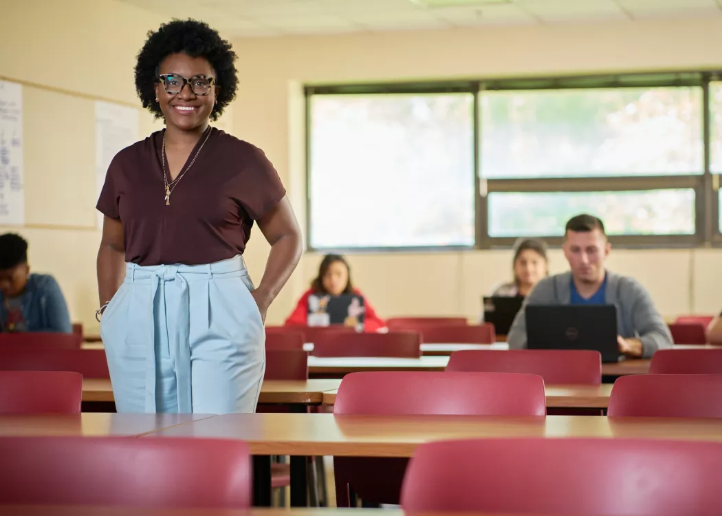 Female professor stands in front of her classroom and students posing for the campaign.