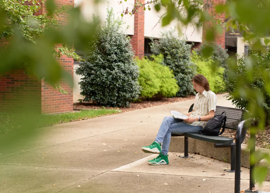 Student sitting on the bench outside the CEHD looking at his academic materials.
