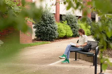 Student sitting on the bench outside the CEHD looking at his academic materials.